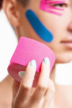 Young woman with facelift taping holding roll of kinesiology tape of pink color. Beauty concept.
