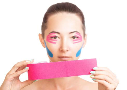 Young woman with facelift and anti-aging taping holding roll of kinesiology pink tape. Beauty concept.