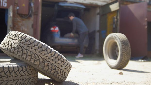 Young man throws away the wheel from his car trunk, close up