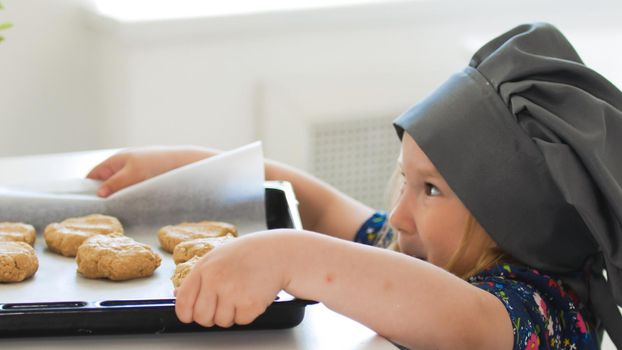 Preschool girl baker holding a baking sheet with cookies, close up