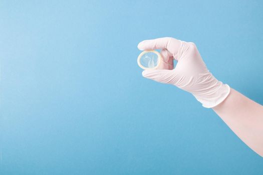hand in a white medical rubber glove holds a condom without packaging on a blue background, copy space