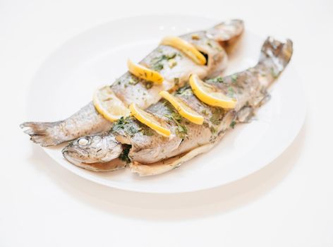 Two baked fish trout dish with lemons and greenery on a white plate.