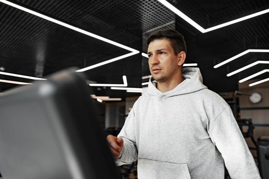 Portrait of a young man in orange windbreaker workout on a fitness machine at a gym.