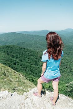 Sporty young woman standing on peak of cliff and enjoying view of summer mountains outdoor.