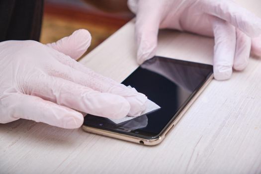a man in rubber gloves wipes the glass of his smartphone with a damp cloth before gluing on the protective glass