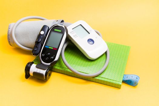 blood pressure monitor and glucose meter on a green notebook, a notebook with a bookmark from a measuring blue tape, control of blood sugar and blood pressure, copy place