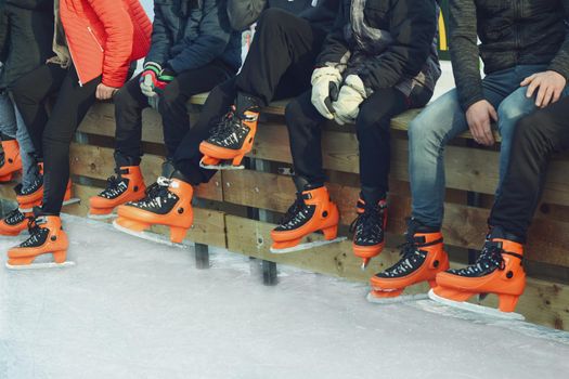 Teenagers in orange skate on the ice.