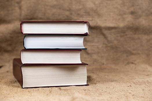 A stack or bound of old books lies on a burlap texture with place for tex