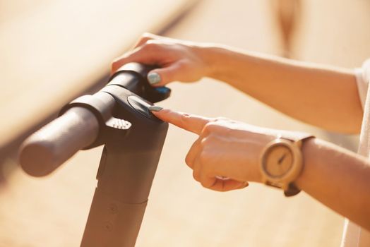 Unrecognizable woman turning on the electric scooter, view of hand.