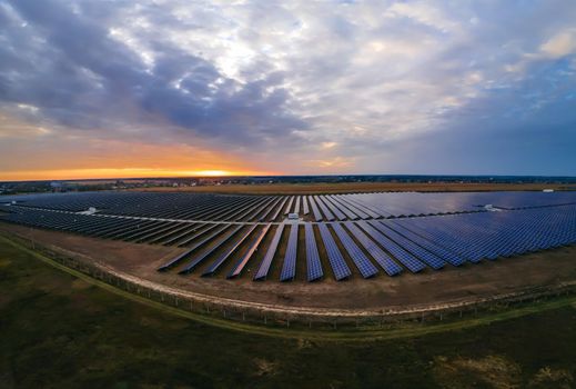 Aerial panorama view of large solar panels at a solar farm at bright summer sunset. Solar cell power plants, colorful photo