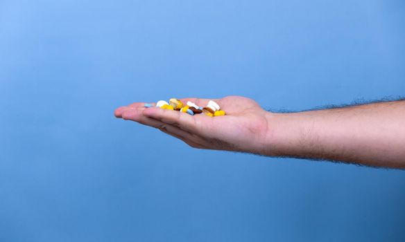 A pile of multi-colored pills in a male hand. A man holds pills in his hand. The concept of medicine, illness, health.