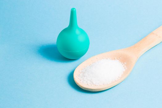 enema for the nose and a wooden spoon with sea salt on a light blue background, copy space, washing the nose with salt water using an aspirator
