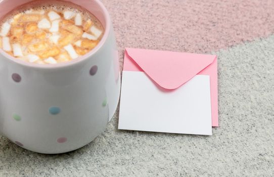 marshmallow cocoa mug and an envelope with a letter on a on pink and beige background. Top view.