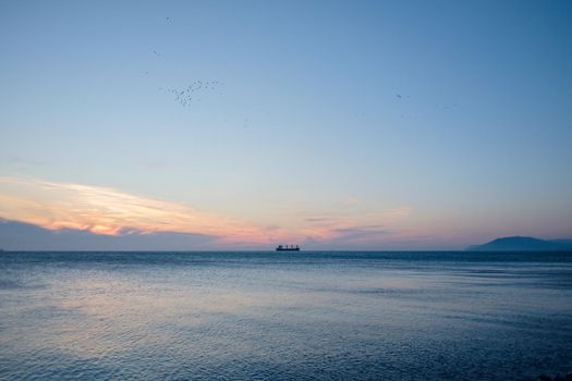 Ship sailing at horizon in the blue sea at sunset.