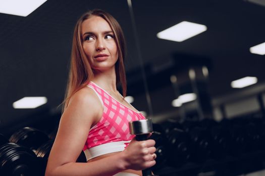 Portrait of a young woman in sportswear posing in a dark gym