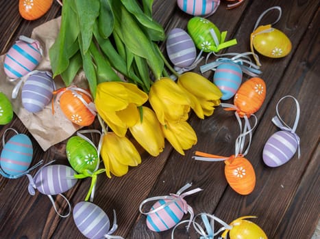 Bouquet of spring yellow tulips and colorful easter eggs on brown wooden background