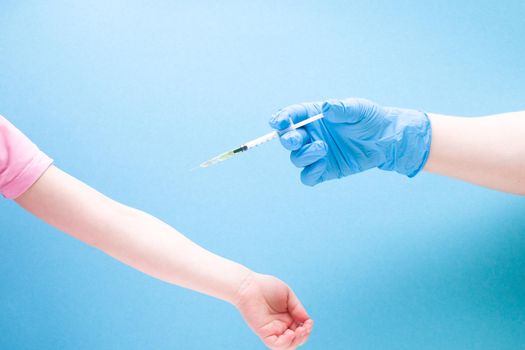 a female hand in a blue rubber medical glove injects a little girl with an insulin syringe on a blue background copy space, treatment and health care concept, child diabetes concept