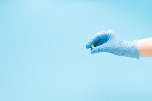 a female hand in a blue rubber medical glove holds a capsule tablet on a blue background copy space, tablet of white and yellow color, treatment and health care concept