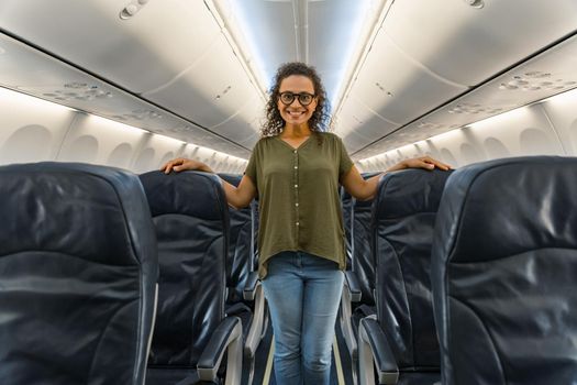 Smiling woman in glasses standing along the rows of seats on the plane. Trip concept
