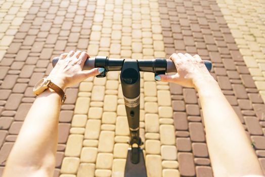 Unrecognizable young woman riding an electric scooter in street outdoor, point of view in first person. Concept of ecological transport.