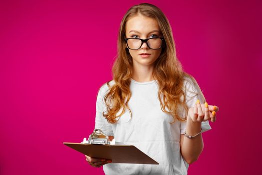 Young beautiful smiling woman standing and holding clipboard against pink background