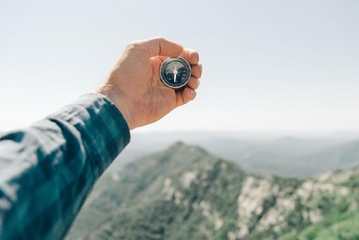 Explorer young man holding compass in hand in front of summer mountain ridge, point of view. Concept of hiking and travel.