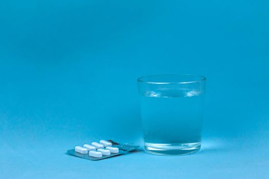 Glass Of Water And Pills On Blue Background with copy space for text.