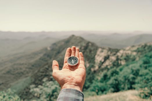 Travel magnetic compass on palm male hand high in summer mountain, point of view.