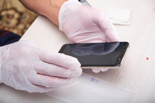 a man in rubber gloves holds a phone he repaired with a new glass on the screen