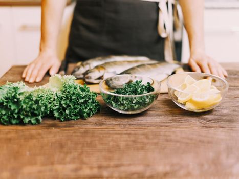 Unrecognizable woman cooking in the kitchen, food ingredients for fish dish on wooden table.