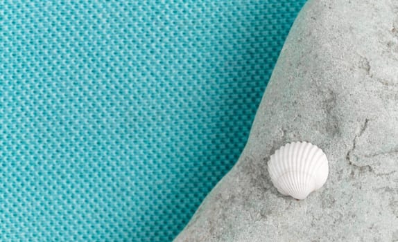 A small white seashell lies on a gray stone. Blue aqua trendy fabric background with empty place for text