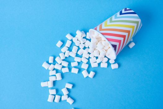 marshmallows dropped out of their holiday paper cups with geometric pattern on blue background, copy space