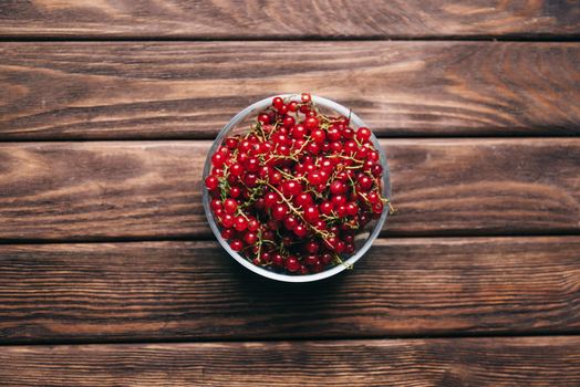 Fresh red currant in a bowl on a wooden background, top view.