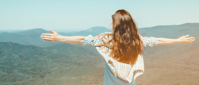 Unrecognizable happy explorer young woman standing with raised arms high in summer mountains outdoor. Image with sunlight effect.