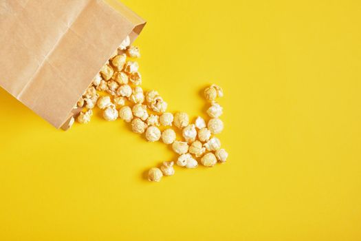 Caramel popcorn in a paper bag on yellow background.copy space top view