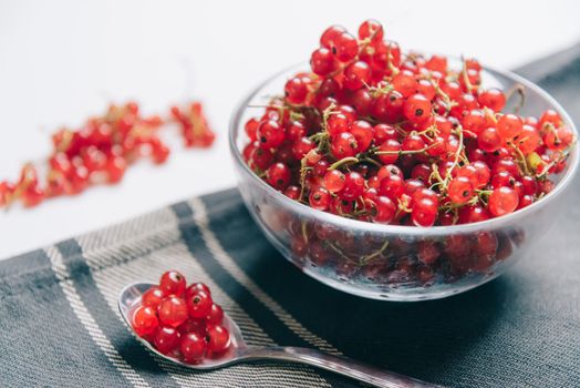 Fresh red ripe currant in a glass bowl and on spoon on napkin.