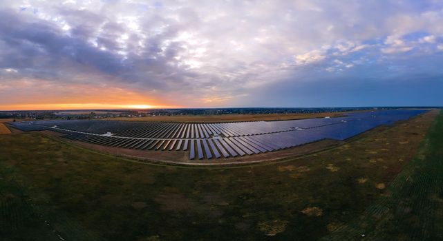 Aerial panorama view of large solar panels at a solar farm at bright summer sunset. Solar cell power plants, colorful photo