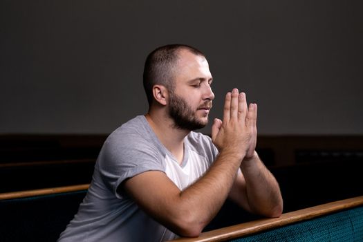 A Christian man in white shirt is sitting and praying with humble heart in the church.