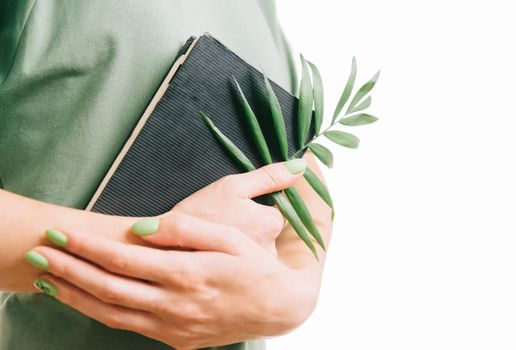 Unrecognizable woman with green manicure holding a notepad and palm leaf.