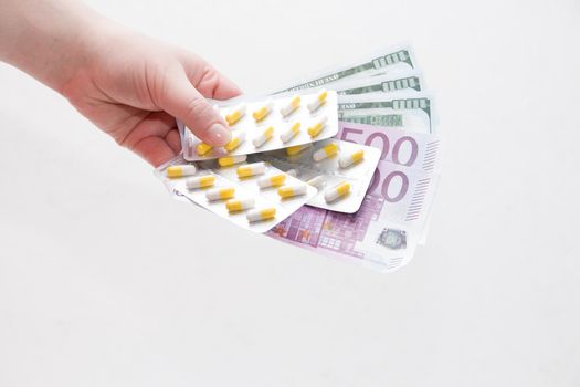 female hand holds packaging yellow capsule pills and dollar bills euro and dollars, white background