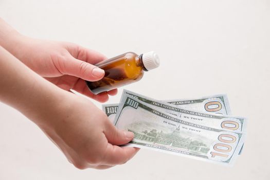 female hands holding a bottle of medicine and dollars notes on a white background