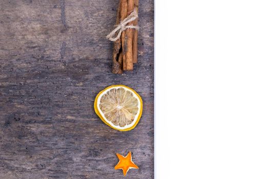 A pile of cinnamon sticks, dried orange and tangerine stars on old wooden table with white empty piece of paper. Christmas decoration. Christmas card.