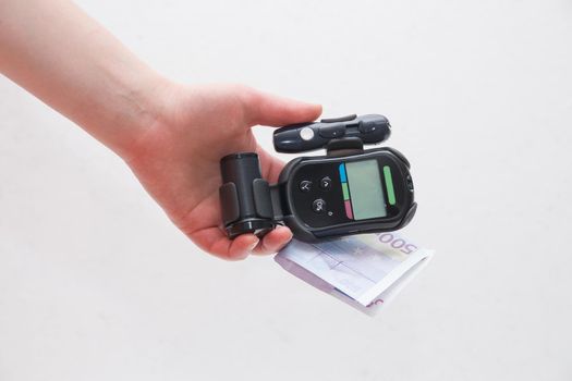 female hand holds a black glucometer and 500 euro white background