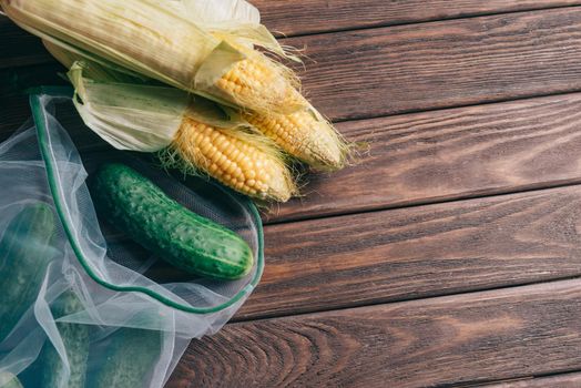 Fresh vegetables: corn and cucumber in reusable eco mesh bags on a wooden background. Zero waste and free plastic concept. Copy-space in right part of image.