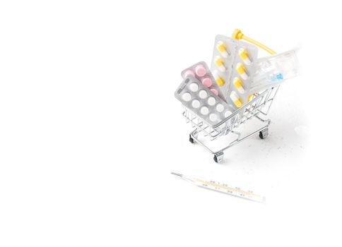 medicines in a shopping trolley and mercury thermometer on a white background copy space