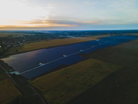 Aerial drone view into large solar panels at a solar farm in large field on countryside at bright sunset. Solar cell power plants, colorful photo