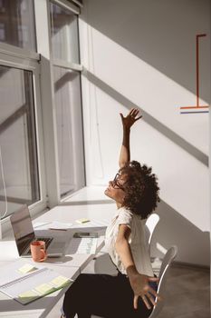 Happy Afro American woman stretching at the desk in the office while sitting near th window