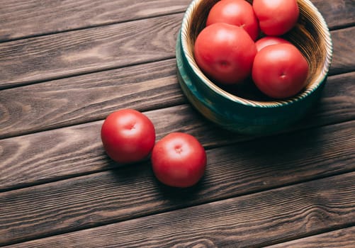 Fresh red ripe tomatoes in a bowl on a wooden table.
