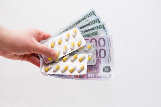 female hand holds packaging yellow capsule pills and dollar bills euro and dollars, white background