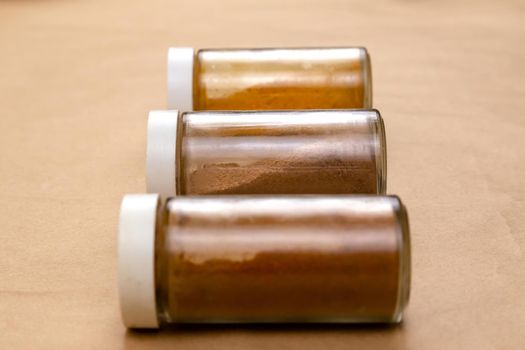 Three jars of seasoning on a brown background with selective focus